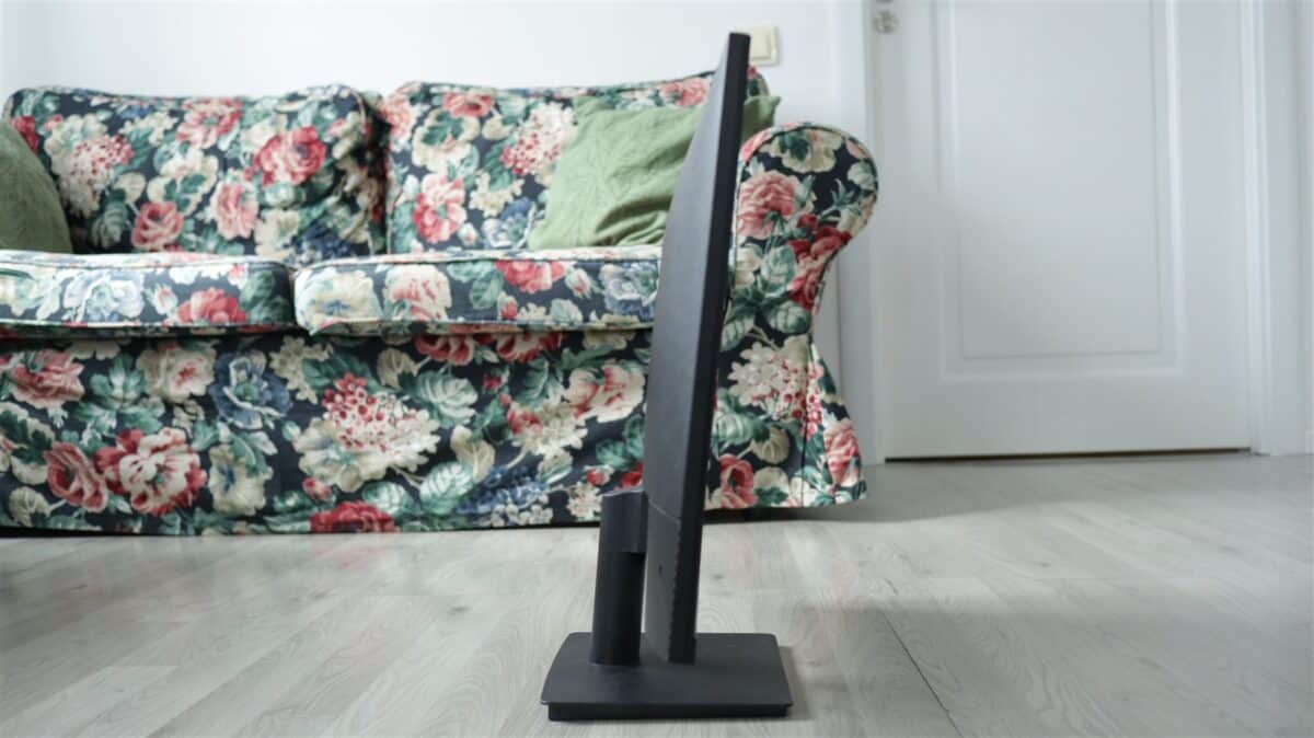 Televizor cu ecran mare și design subțire, plasat în fața unei canapele cu imprimeu floral.